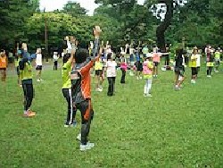 代々木公園練習会の風景（エアロビクスでウォーミングアップする参加者が数十人人写っています）