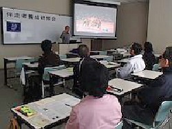 会津大学での研修会・講義の様子(スクリーンに映った動画で伴走の説明する講師と参加者が写っています）