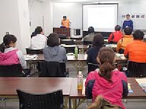 伴走者養成研修会の講義風景(受講者の後ろから写しています。受講者は10人ほど見え、プロジェクタのスクリーンと講師の姿が写っています)